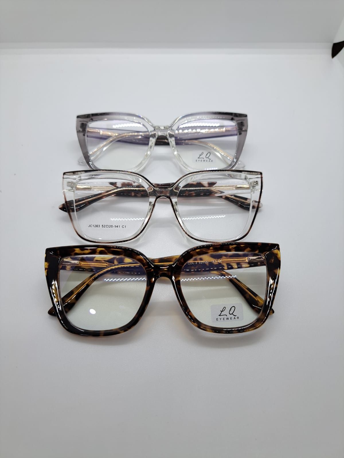 Tres pares de gafas con montura transparente y estampada, dispuestas verticalmente sobre una superficie blanca.