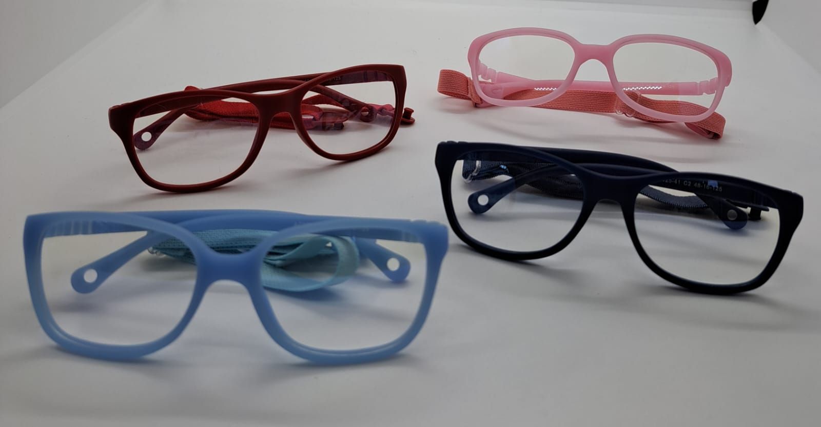 Cuatro pares de anteojos: marcos rojo, rosa, azul y negro sobre una superficie blanca.