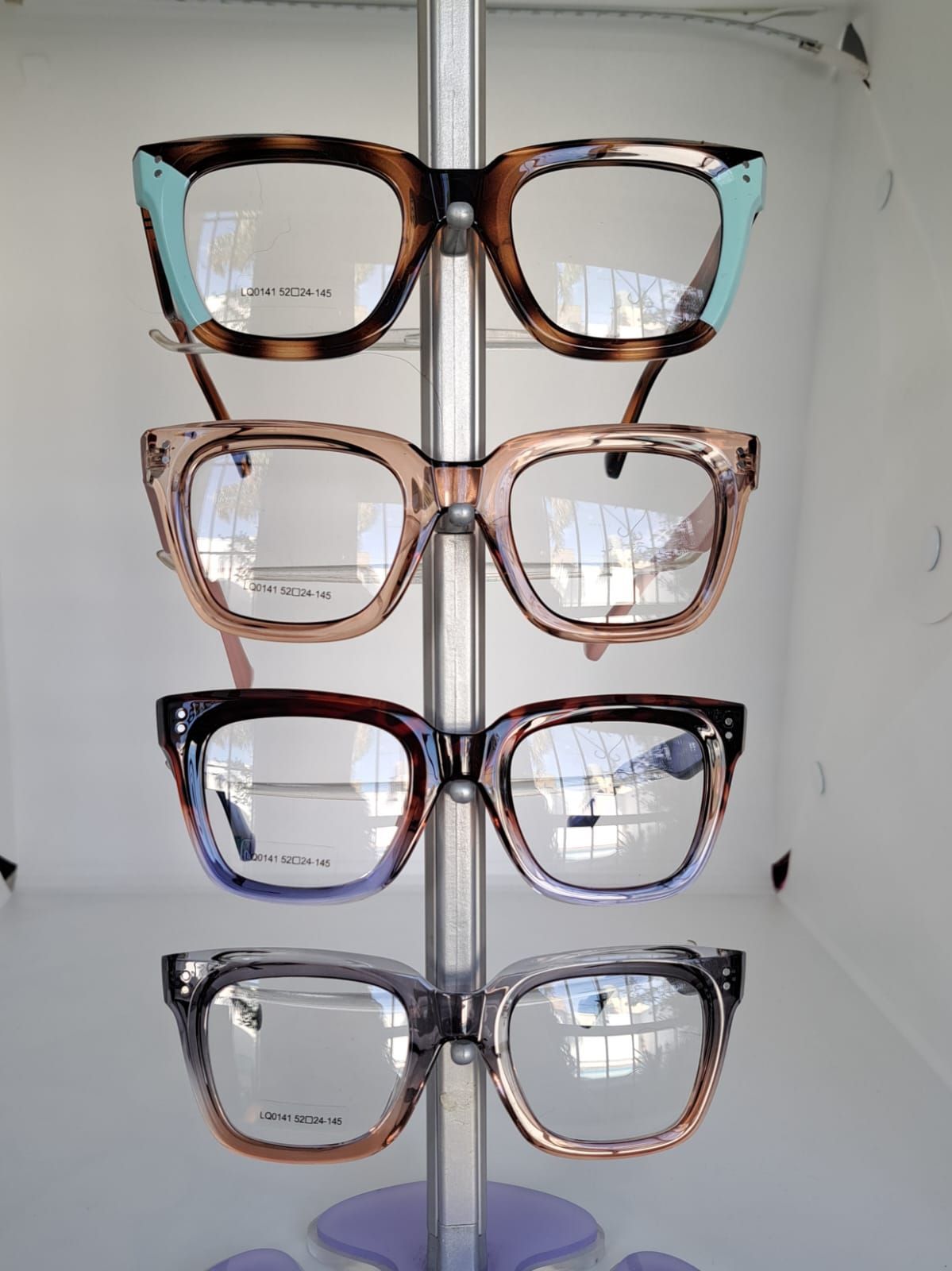 Cuatro pares de gafas expuestas en un expositor vertical. Las monturas son de varios colores