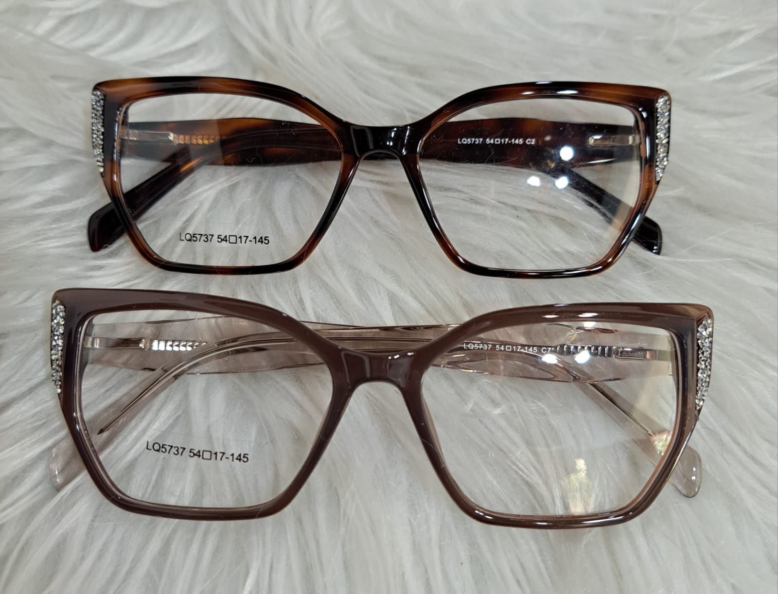 Dos pares de gafas con diseño de carey y lentes cuadradas, expuestas sobre una superficie blanca esponjosa.