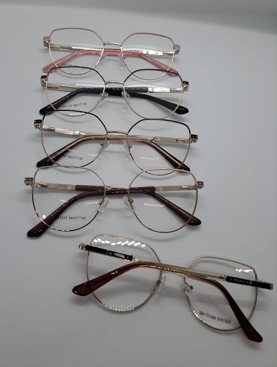 Cinco pares de gafas, con monturas de distintas formas y colores, dispuestas sobre una superficie blanca.