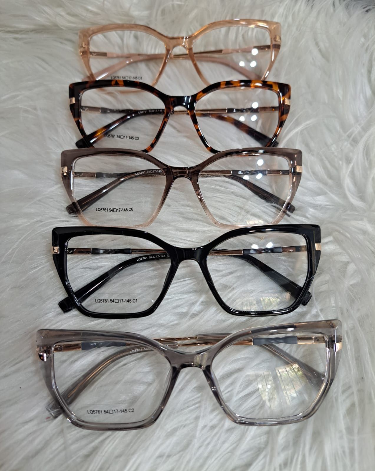 Cinco pares de anteojos en varios colores y estilos dispuestos sobre una superficie blanca y esponjosa.