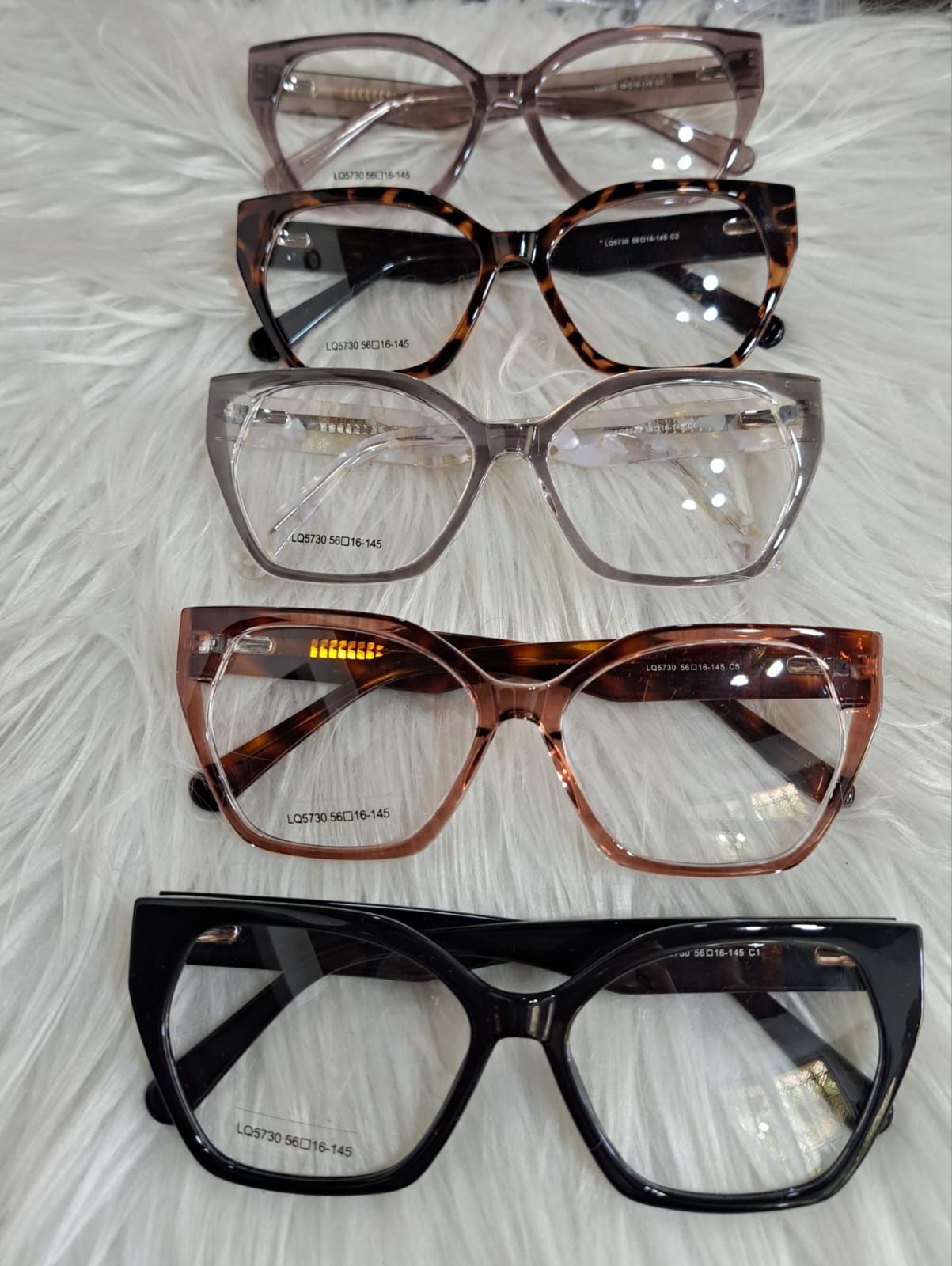 Cinco pares de anteojos con marcos de diferentes colores exhibidos sobre una superficie blanca y esponjosa.