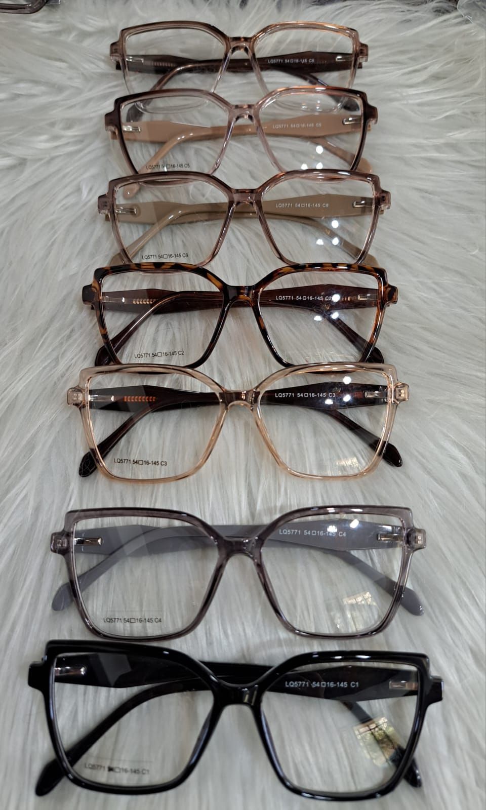 Monturas de gafas dispuestas verticalmente sobre una superficie blanca texturizada. Se aprecian diversas formas y colores.