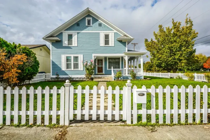 White vinyl picket fence in front of a blue residential home