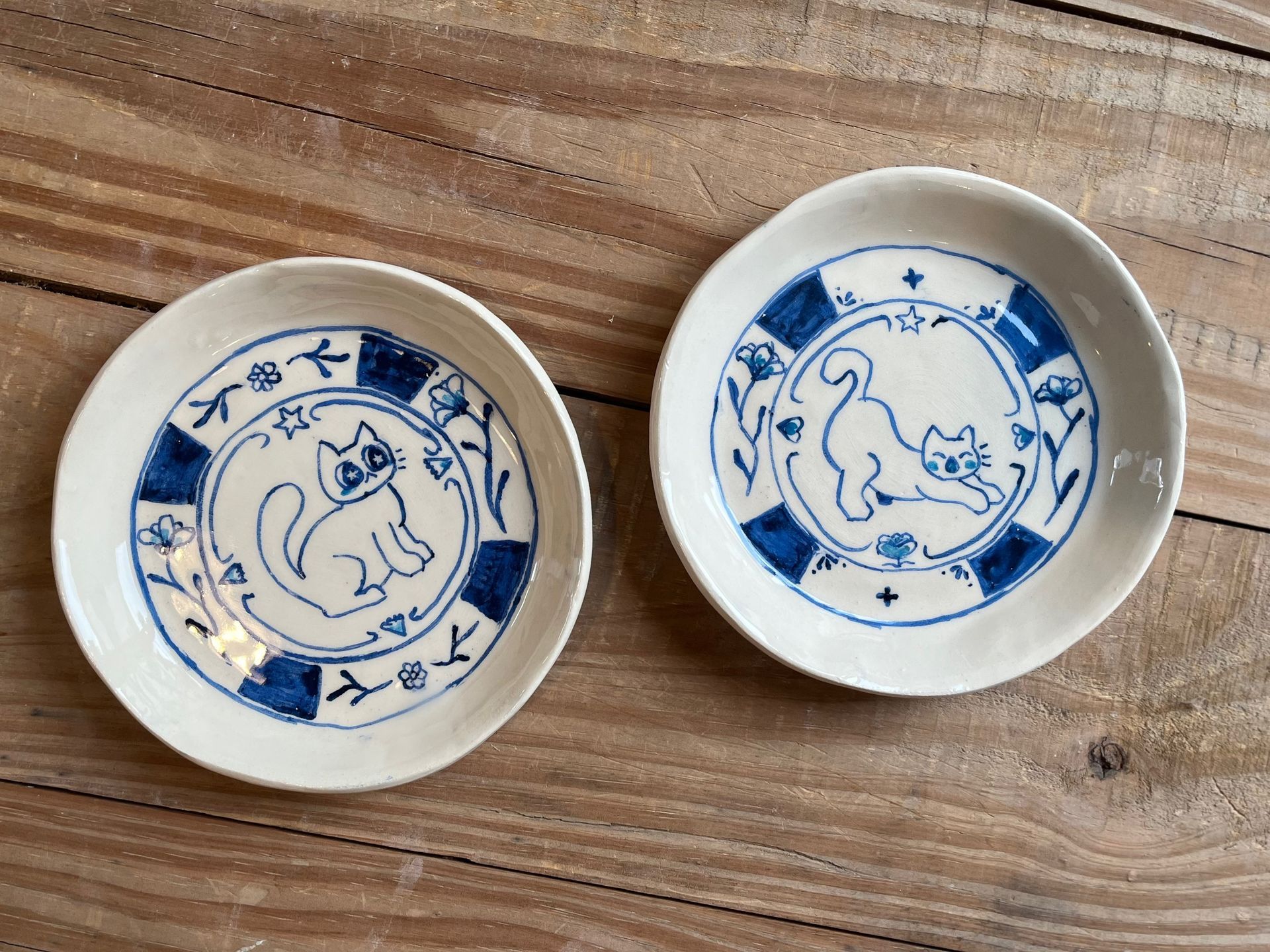 Dos platos de cerámica blanca con ilustraciones y bordes de gatos azules.