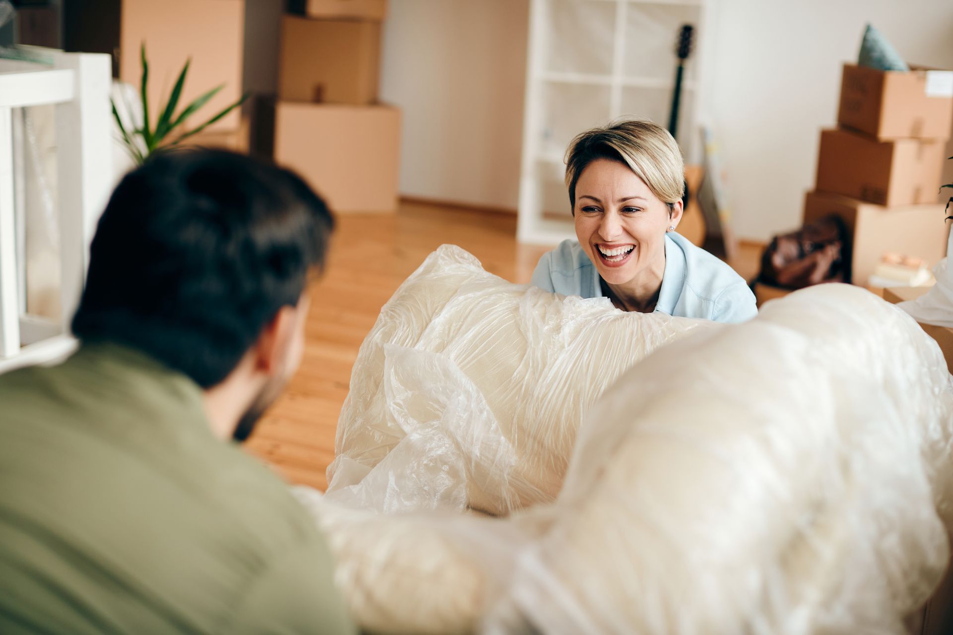 A man and a woman are sitting on a couch wrapped in plastic.