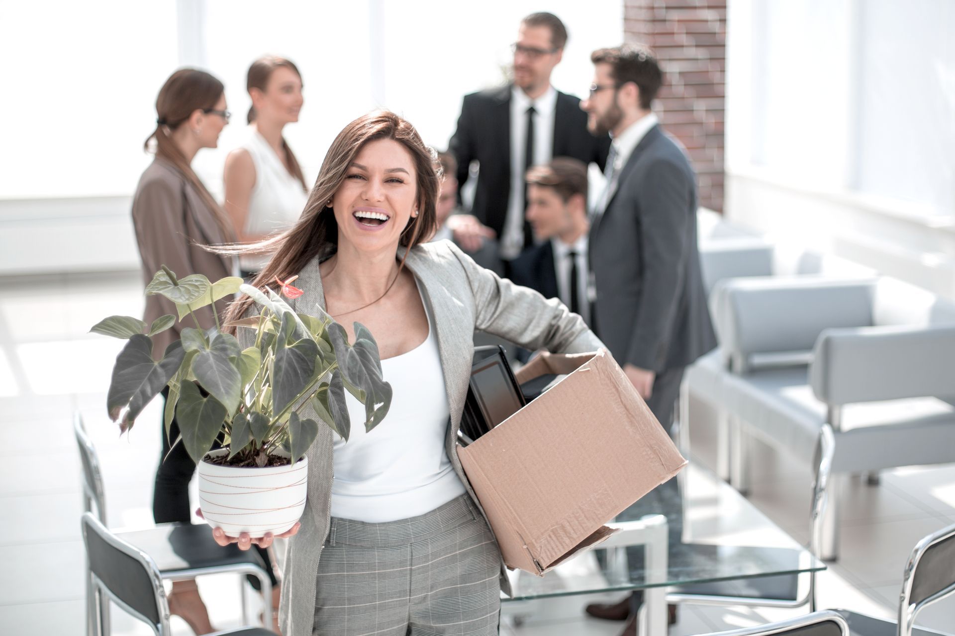 A woman is holding a potted plant and a box of her belongings.