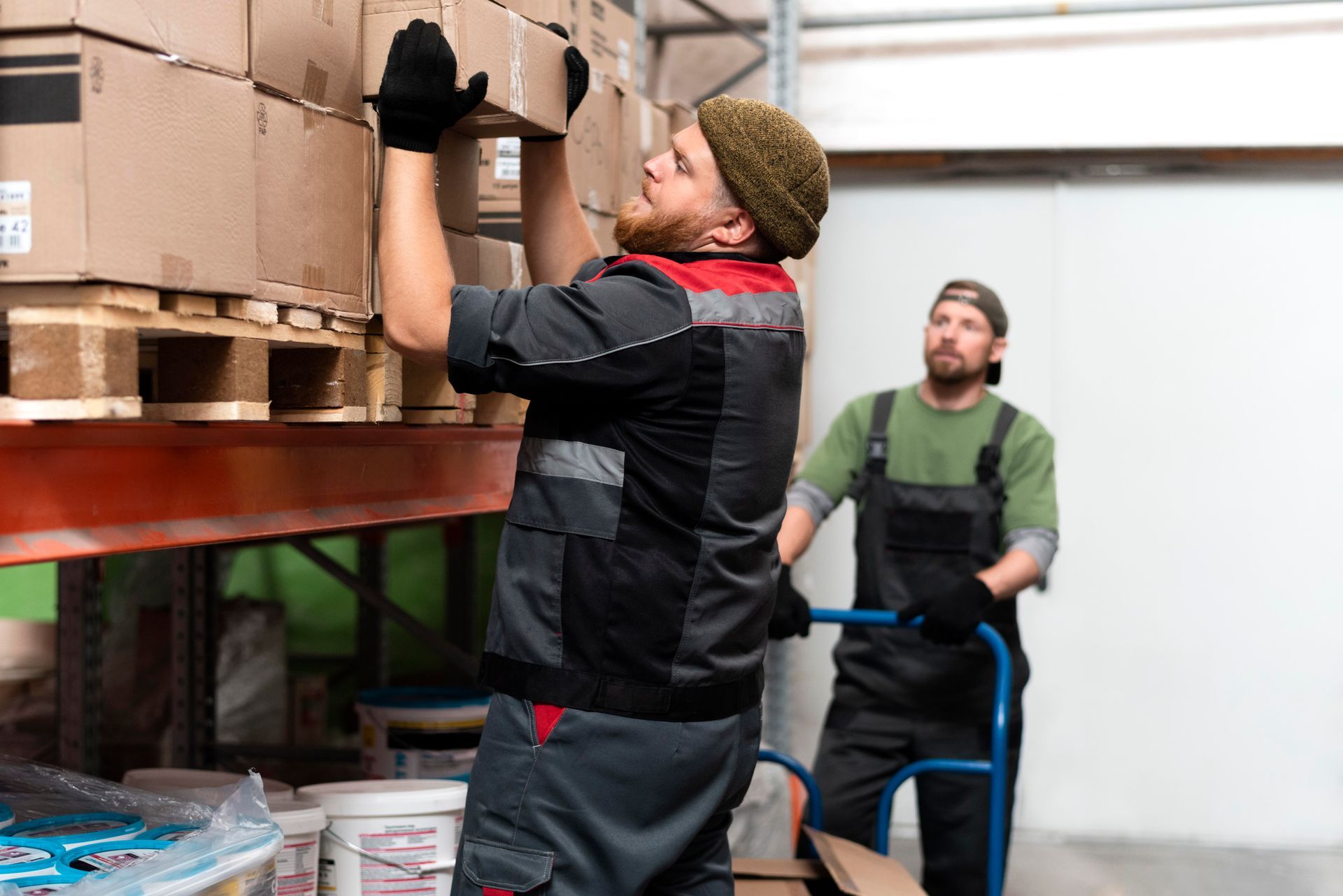 Two men are working in a warehouse loading boxes on pallets.