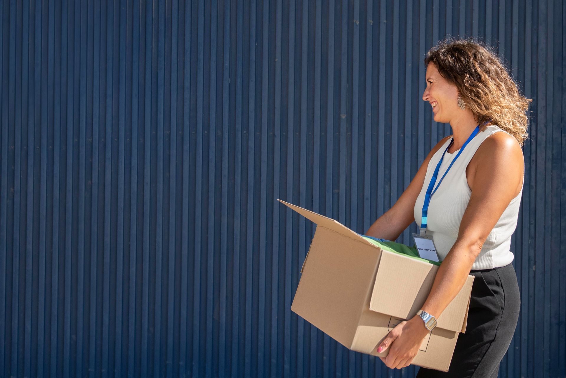 A woman is carrying a cardboard box in front of a blue wall.