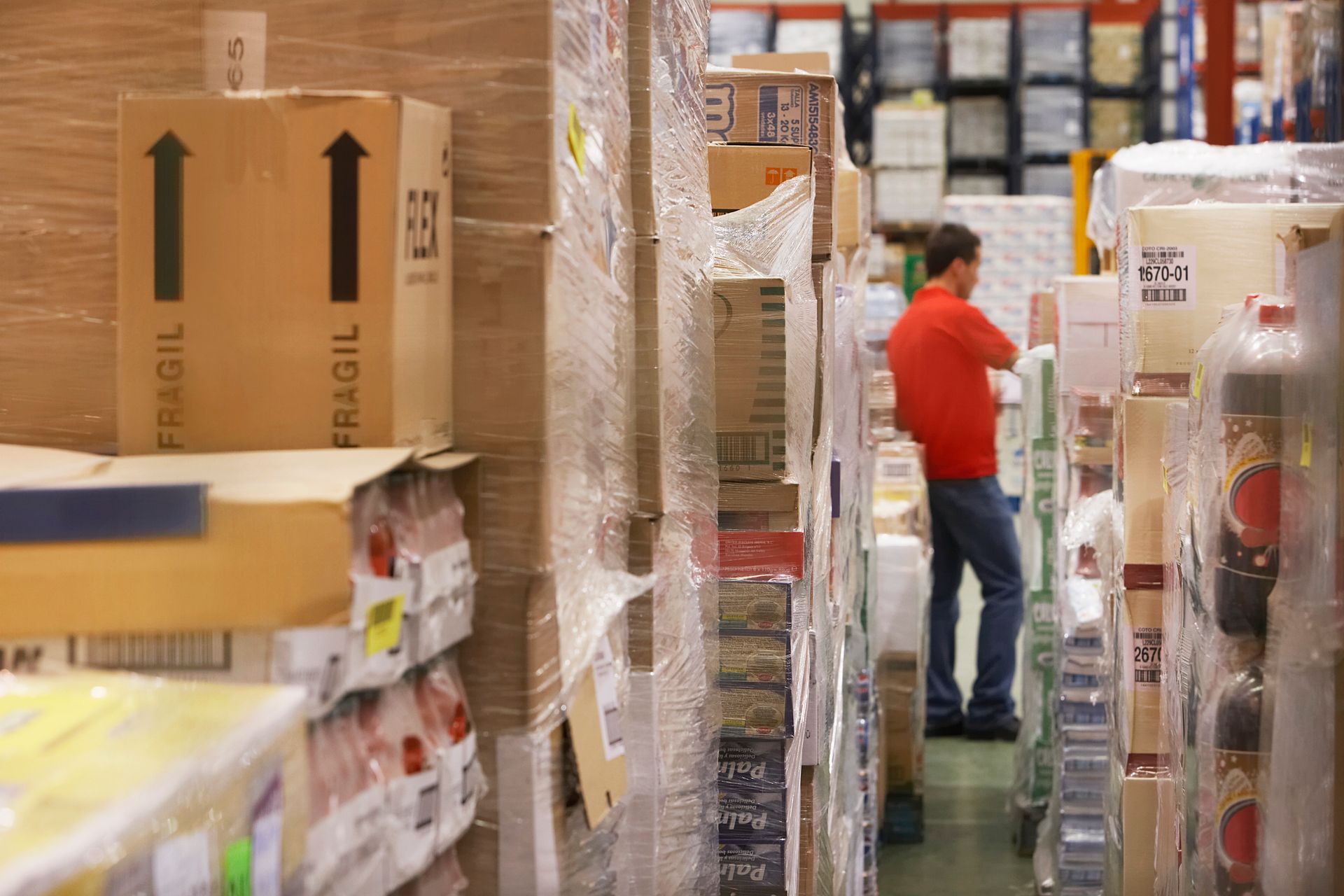 A man in a red shirt is standing in a warehouse filled with lots of boxes.