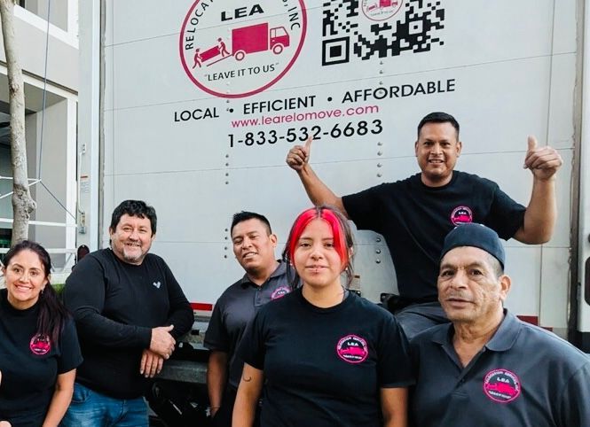 Six people in black shirts pose in front of a LEA truck with logo and phone number.