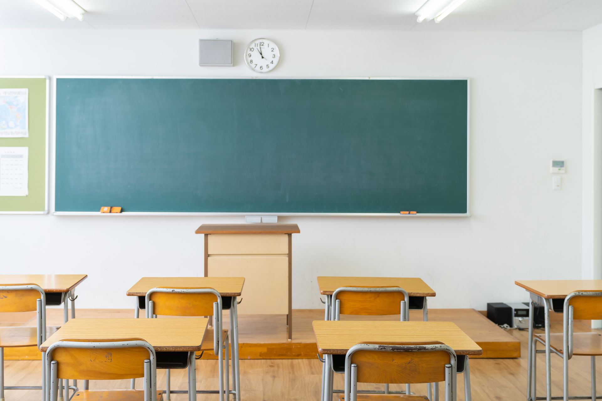 An empty classroom with tables and chairs and a blackboard.