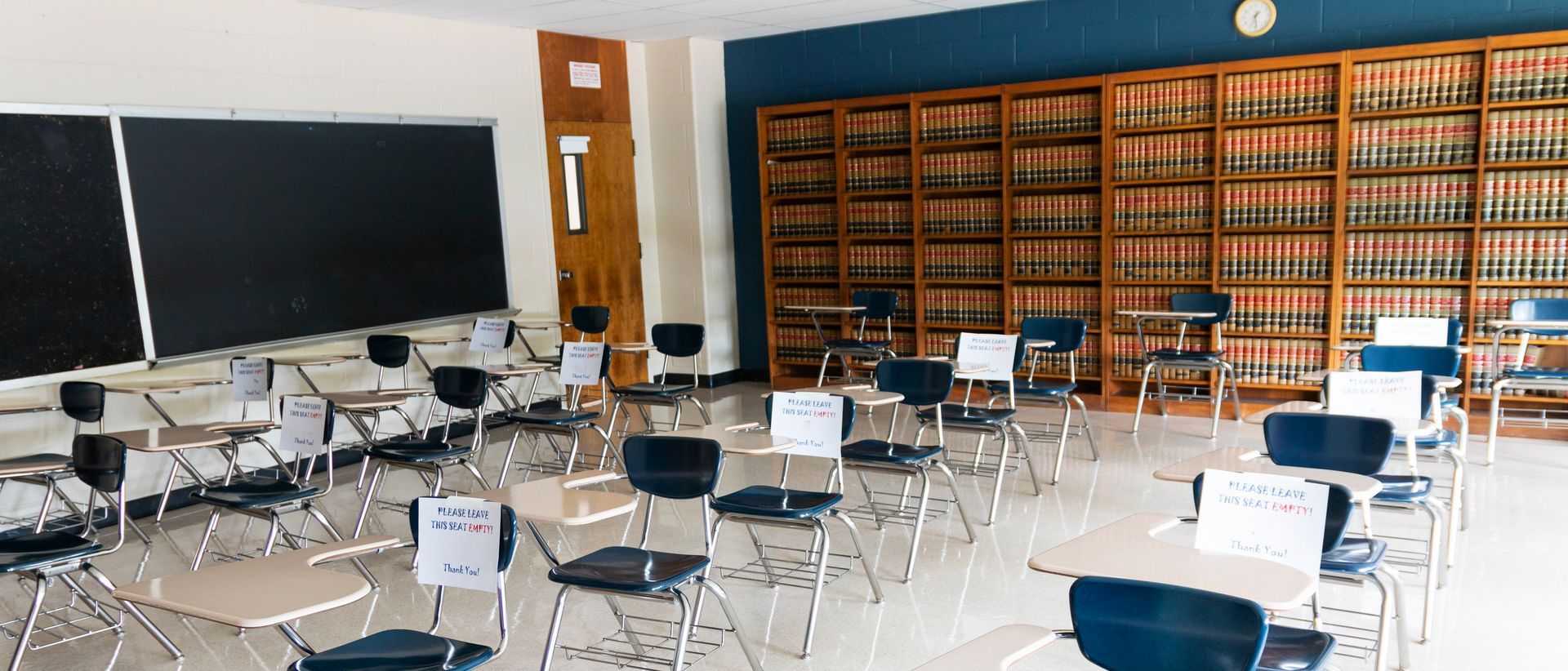 An empty classroom with tables and chairs and a clock on the wall