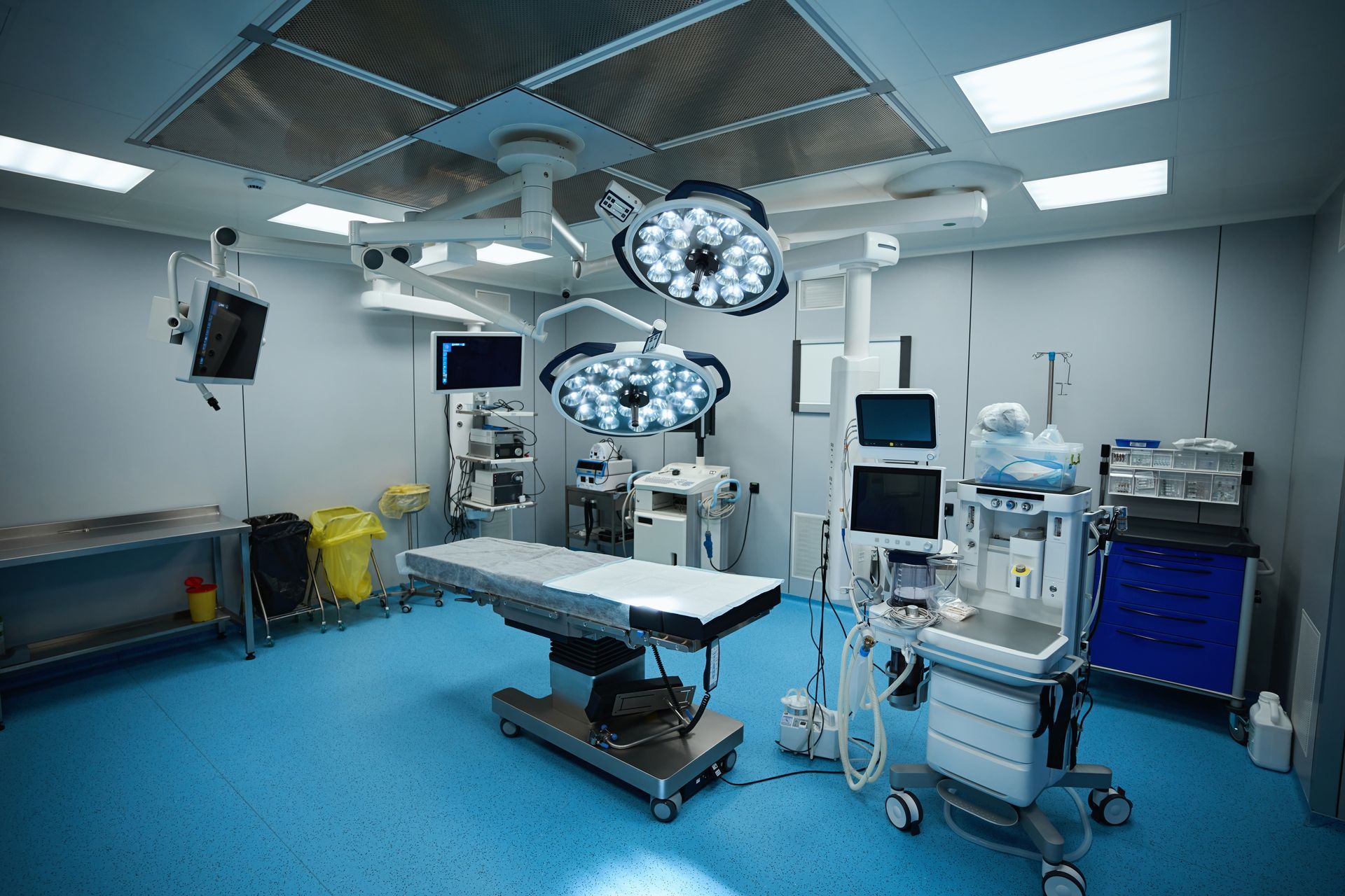 An empty, modern operating room with surgical lights, equipment, and a blue floor.