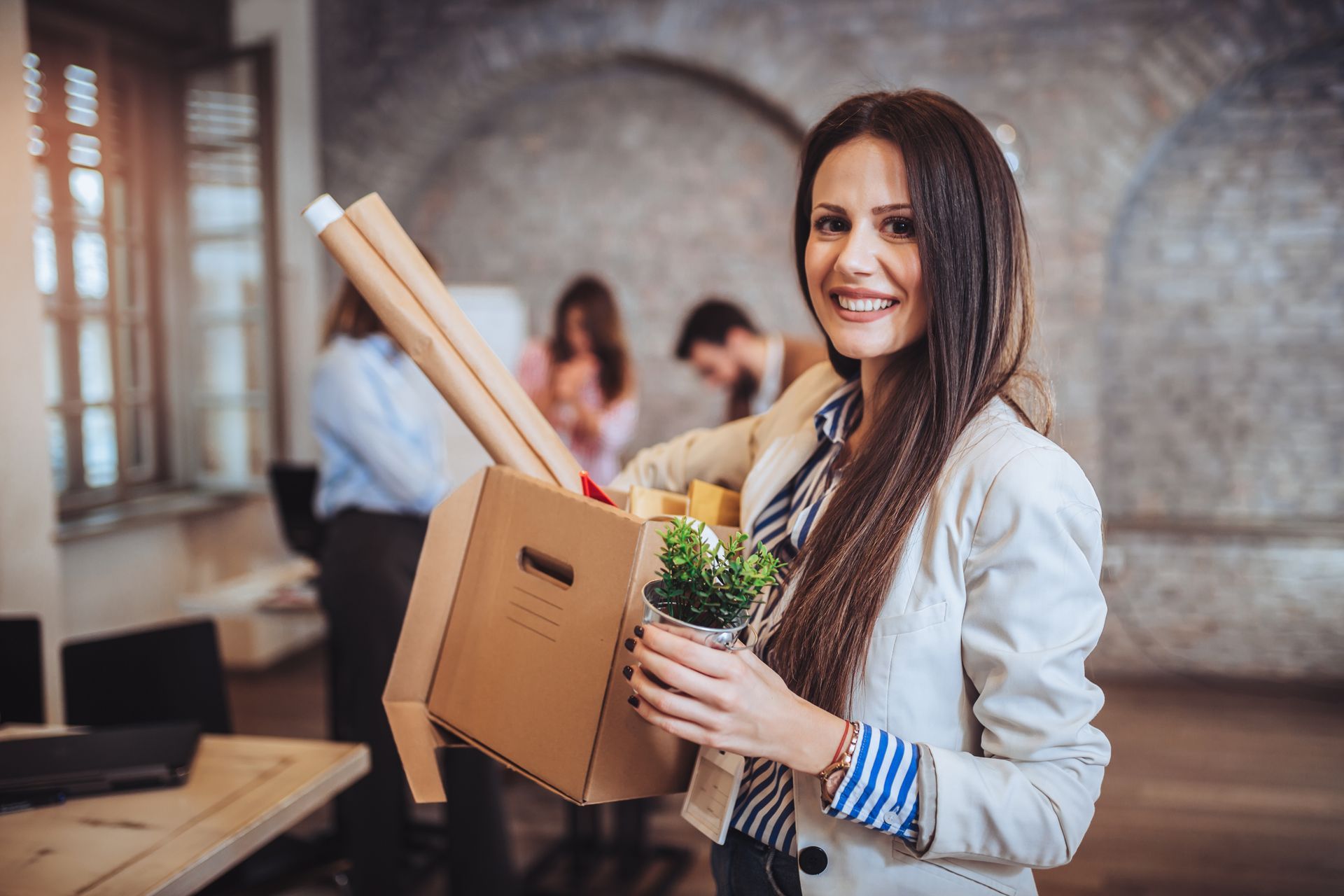 A woman is holding a box of her belongings in an office.