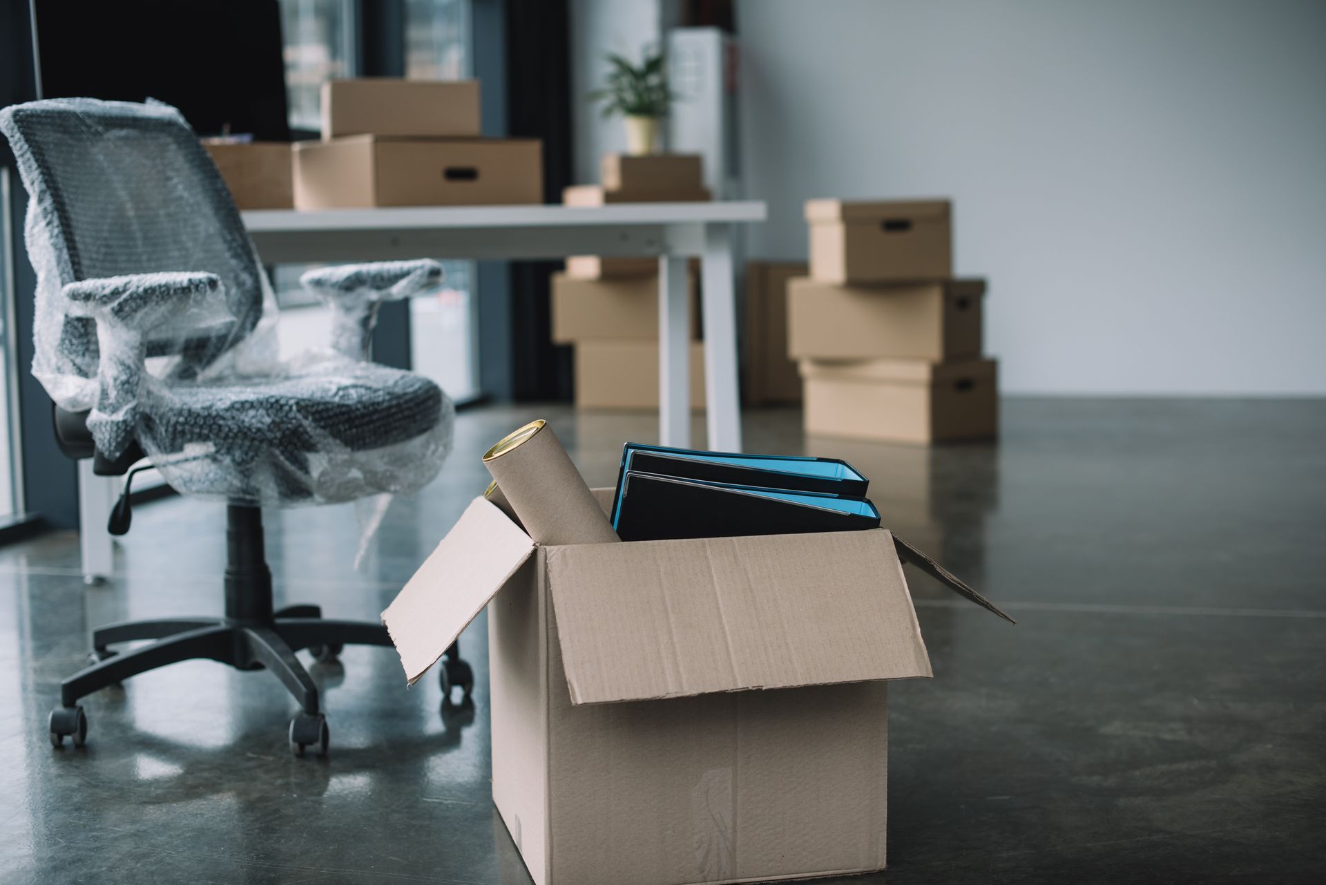 An office chair is wrapped in plastic next to a cardboard box.