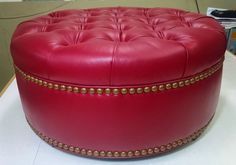 A red leather ottoman is sitting on top of a white table.