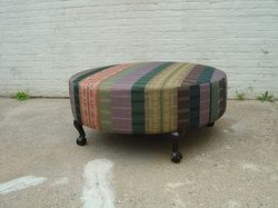 A colorful striped ottoman is sitting on the ground in front of a white brick wall.