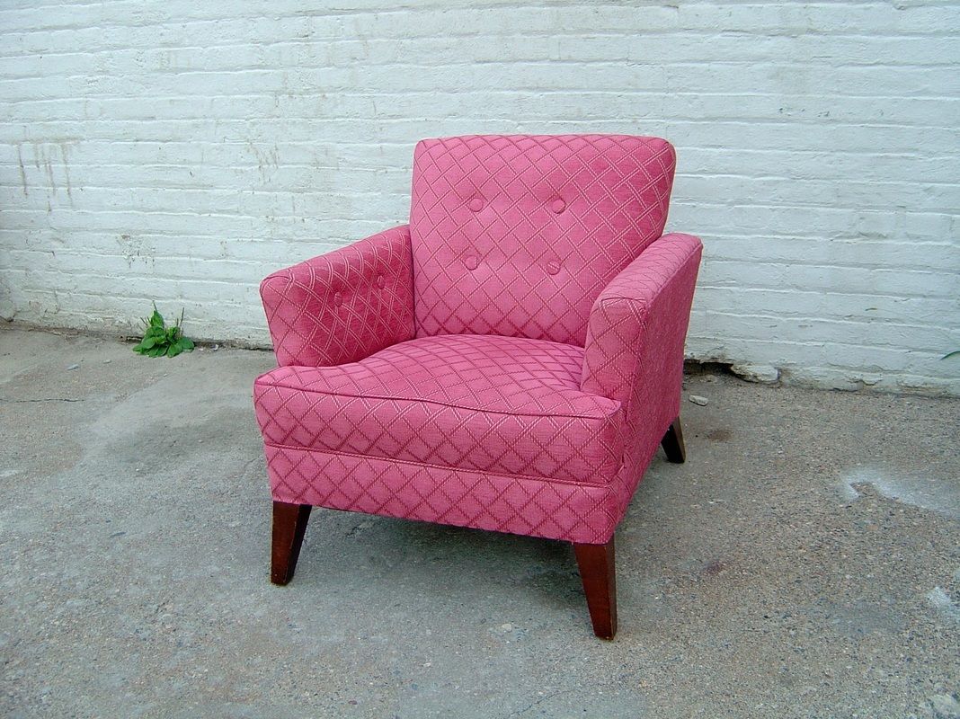 A pink chair is sitting in front of a white brick wall.