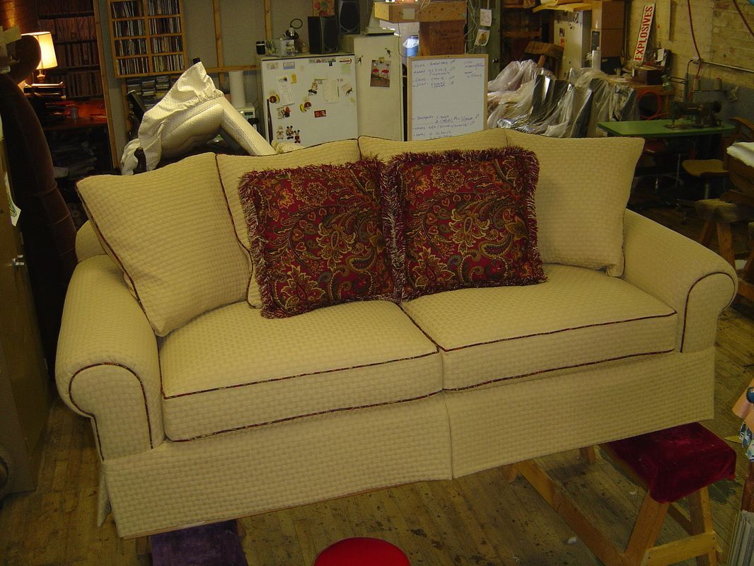 A beige couch with two red pillows on it