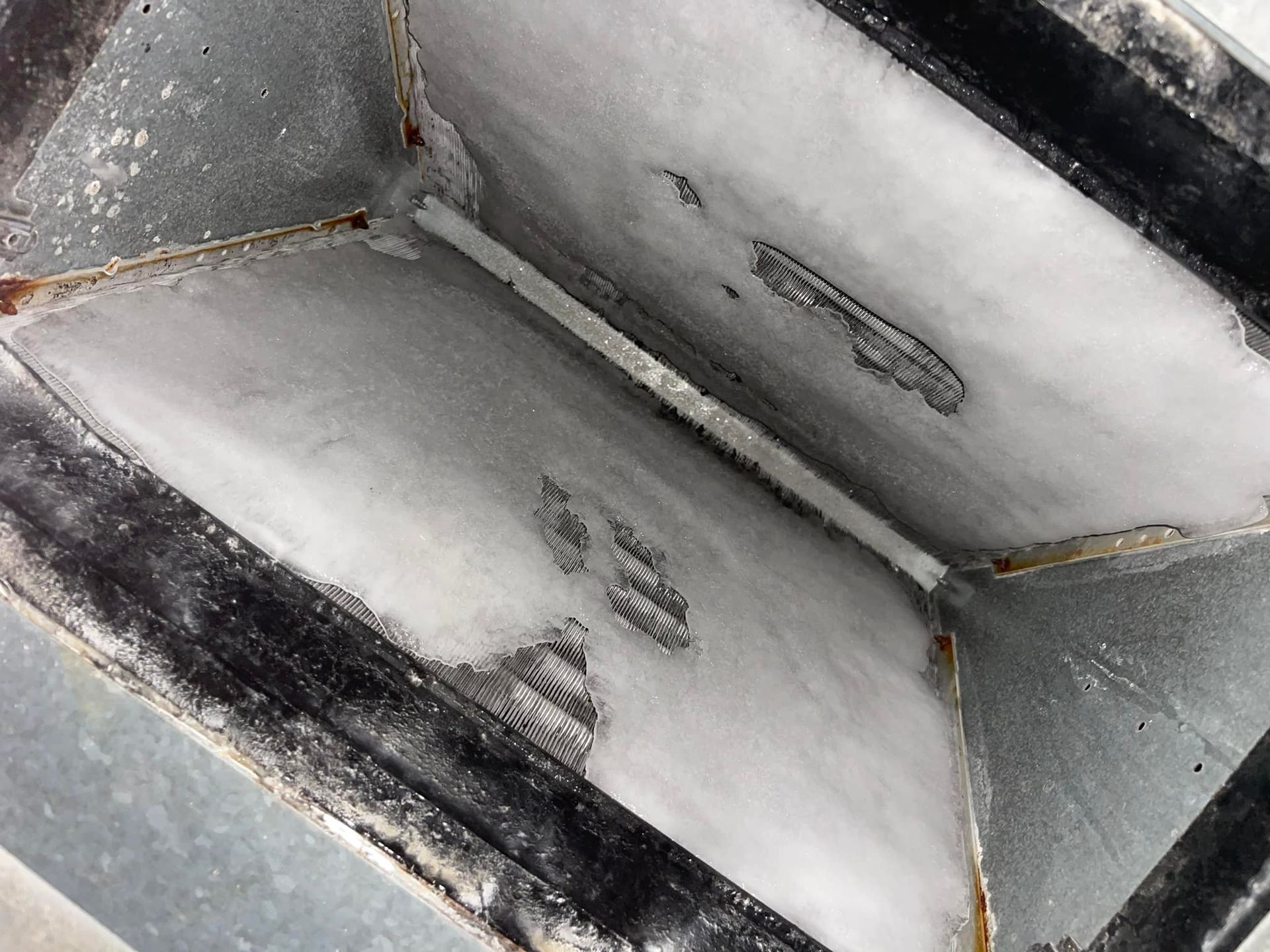 Close-up view of a dusty, rectangular metal duct interior, coated in a white substance.