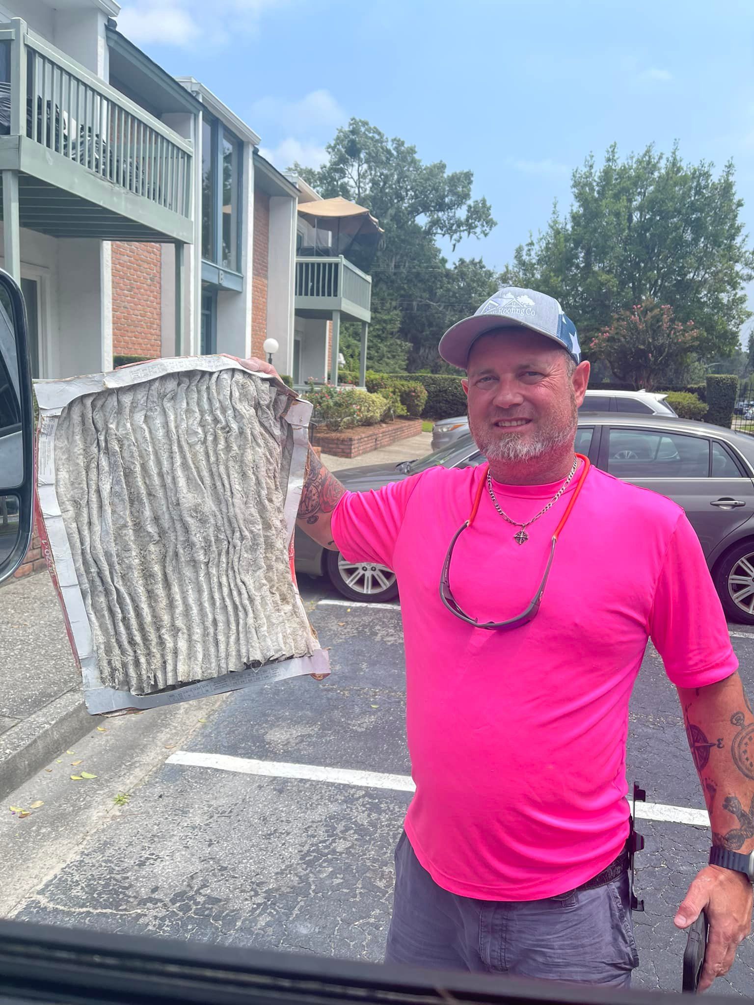 A person in a pink shirt examines an air conditioning unit attached to a building, with a gas tank nearby.