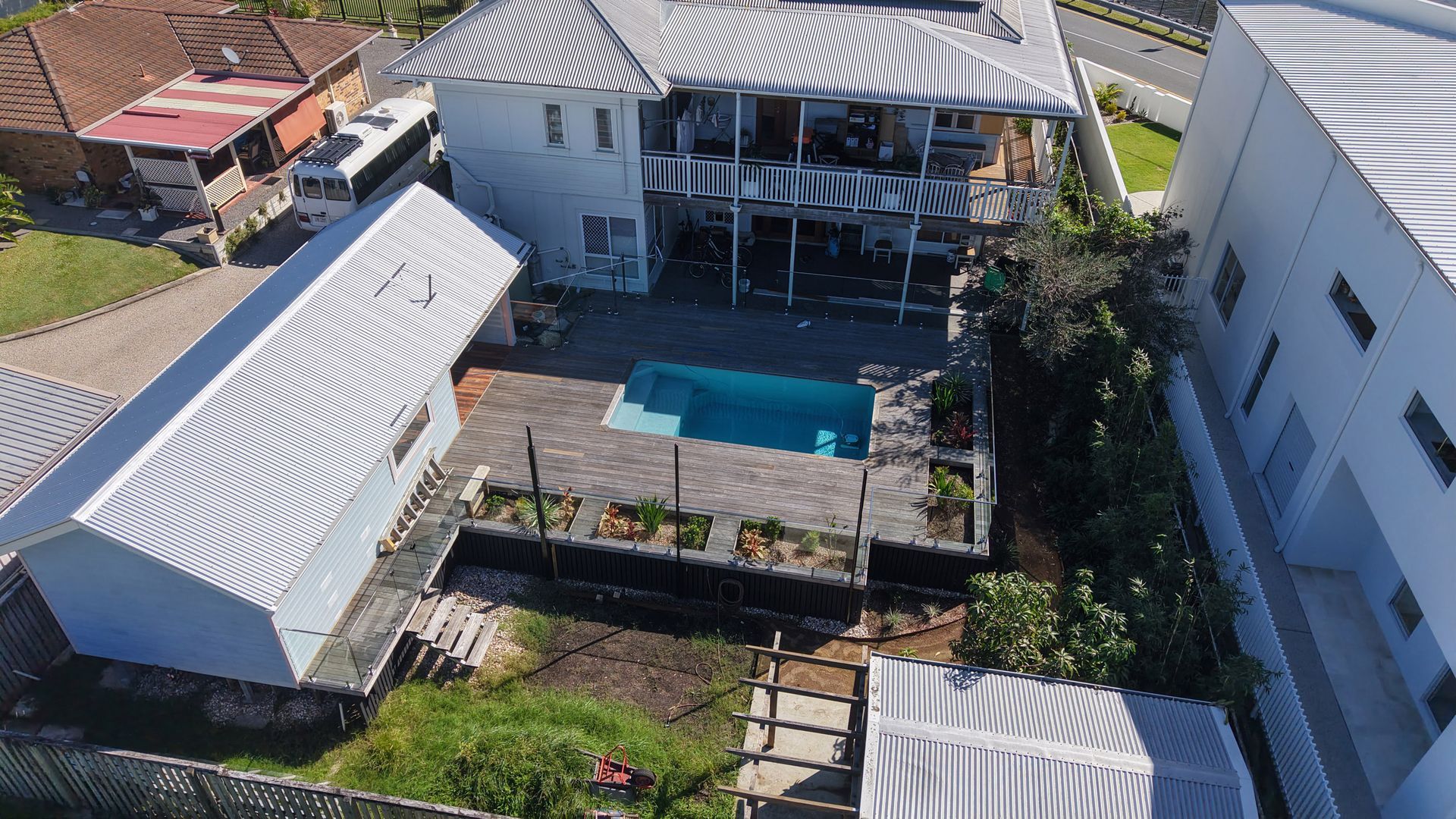 Aerial view of a two-story white house with a pool. A shed is to the left and a neighboring building to the right.