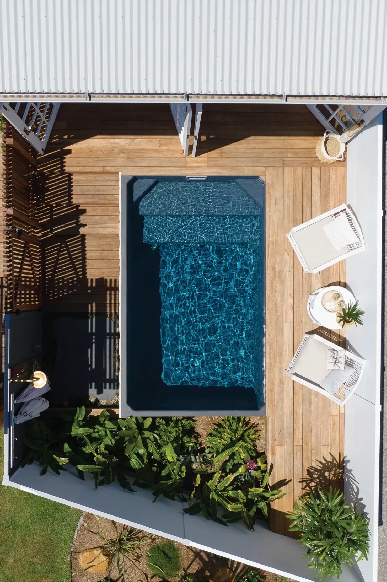 Overhead view of a small pool surrounded by wooden decking, lounge chairs, and landscaping in a sunny backyard.