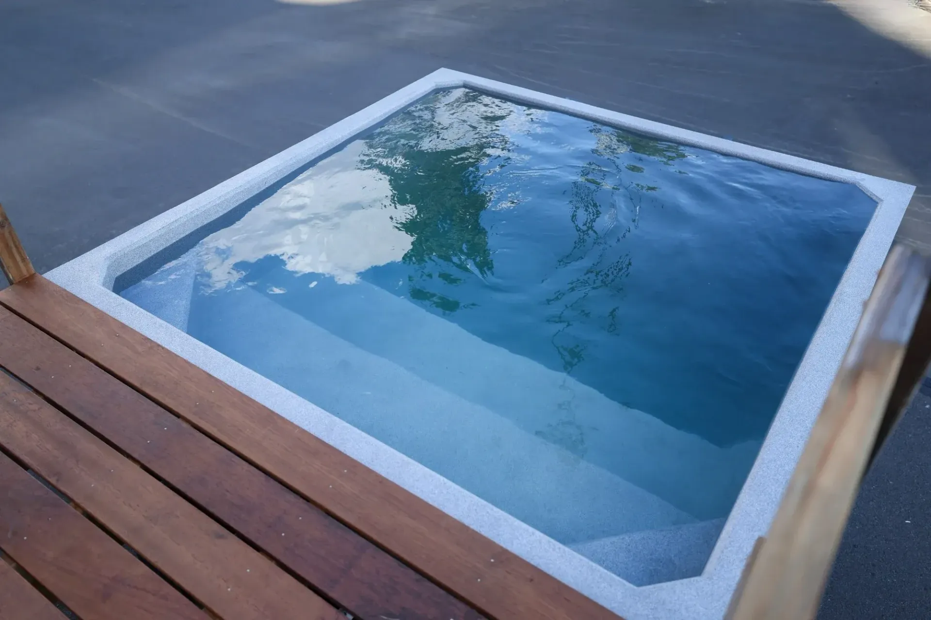 Small square plunge pool with built-in steps, clear water, and a wooden deck.