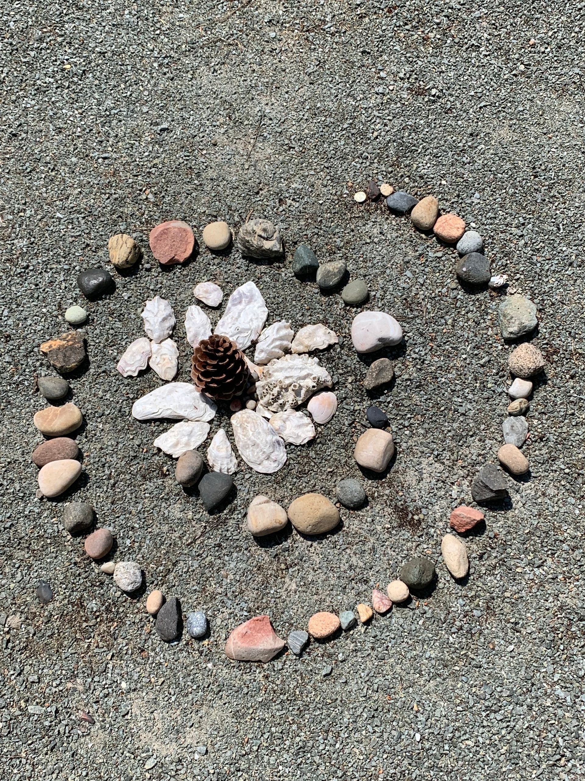 A flower made out of rocks and a pine cone on the ground.