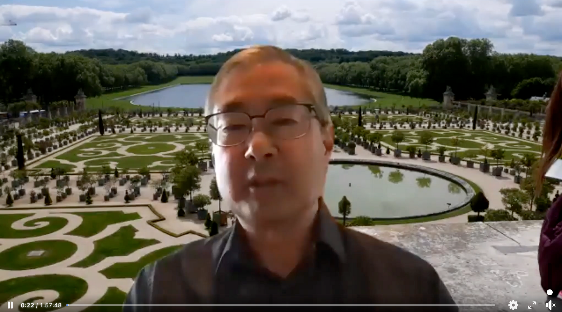 A man wearing glasses is standing in front of a large garden.