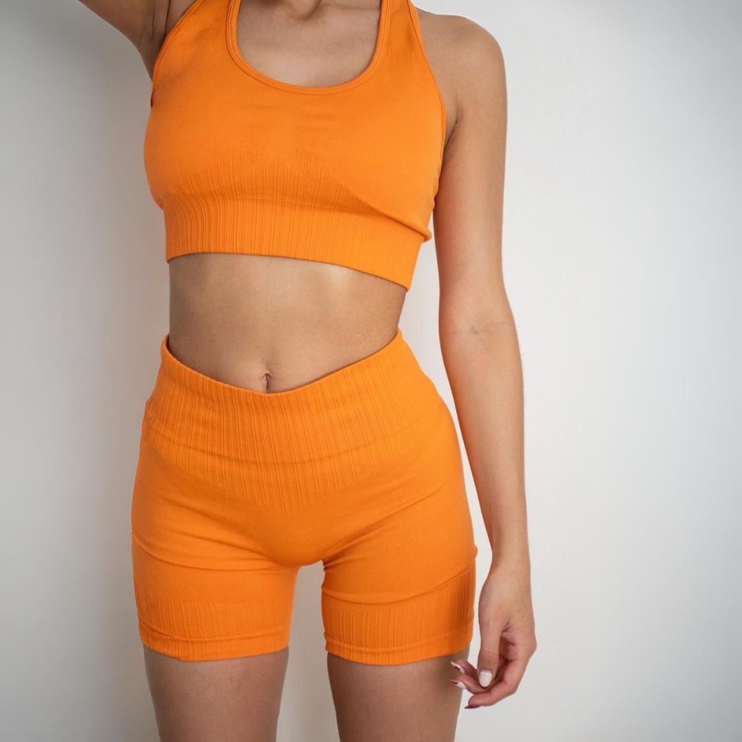 Mujer que lleva un sujetador deportivo y pantalones cortos de color naranja; fondo blanco.