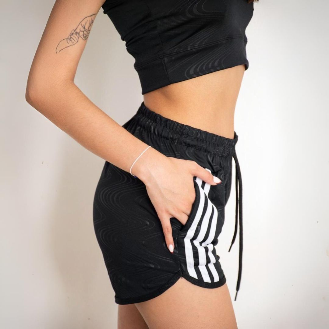 Mujer vestida con sujetador deportivo Adidas negro y pantalones cortos con rayas blancas.