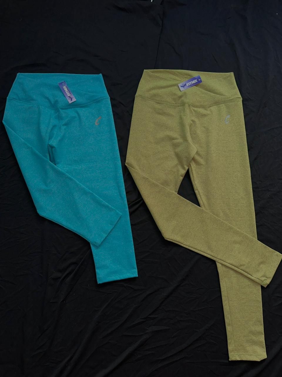 Dos pares de leggings deportivos, uno verde azulado y otro verde oliva, colocados sobre tela negra.