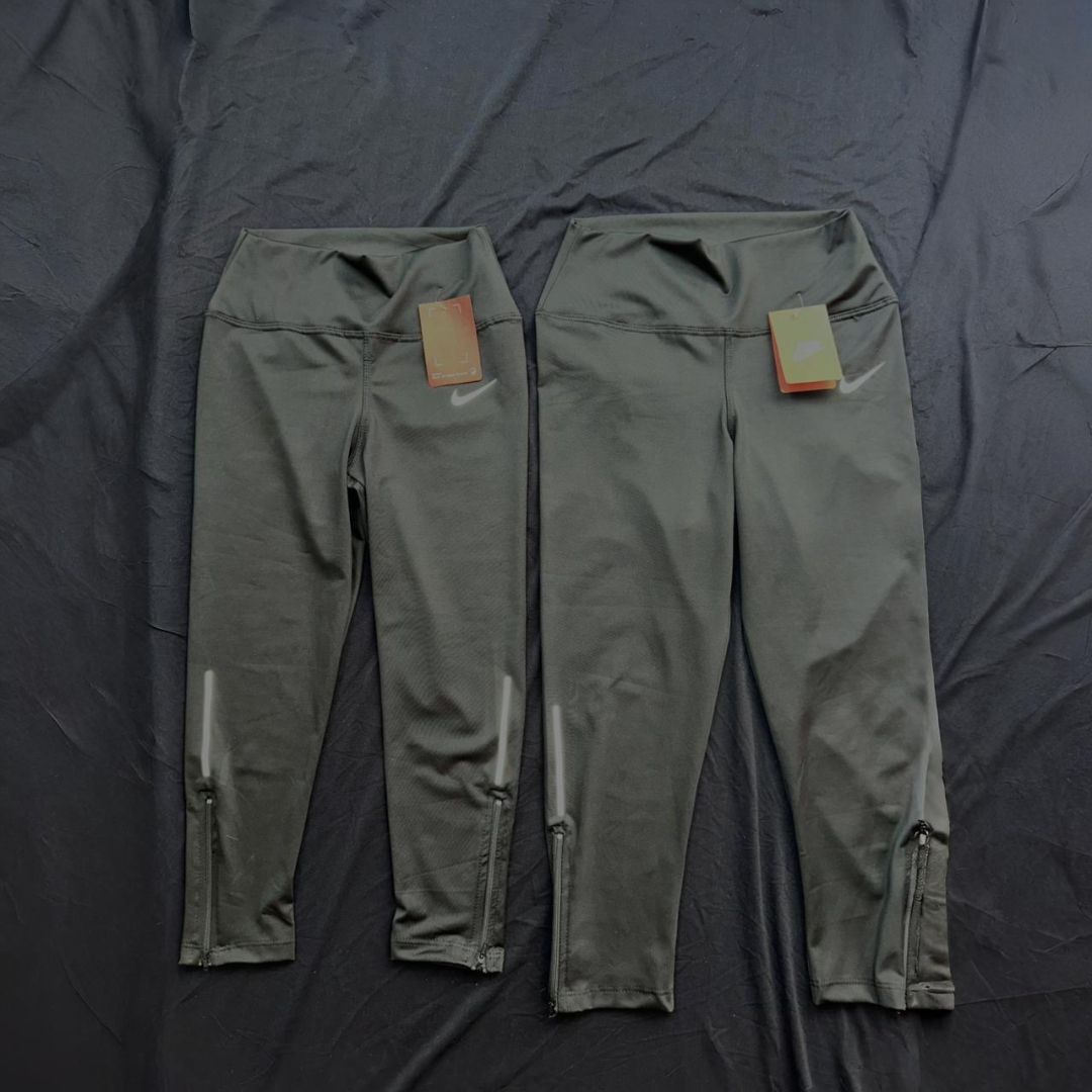 Dos pares de pantalones deportivos Nike de color gris, con etiquetas, colocados sobre una superficie oscura.