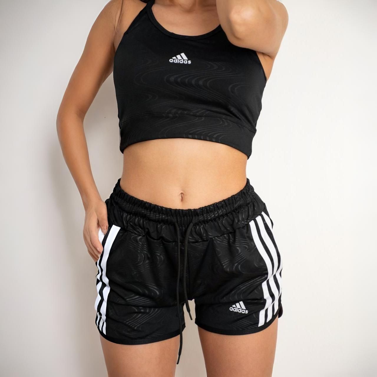 Mujer vestida con sujetador deportivo Adidas negro y pantalones cortos con rayas blancas.