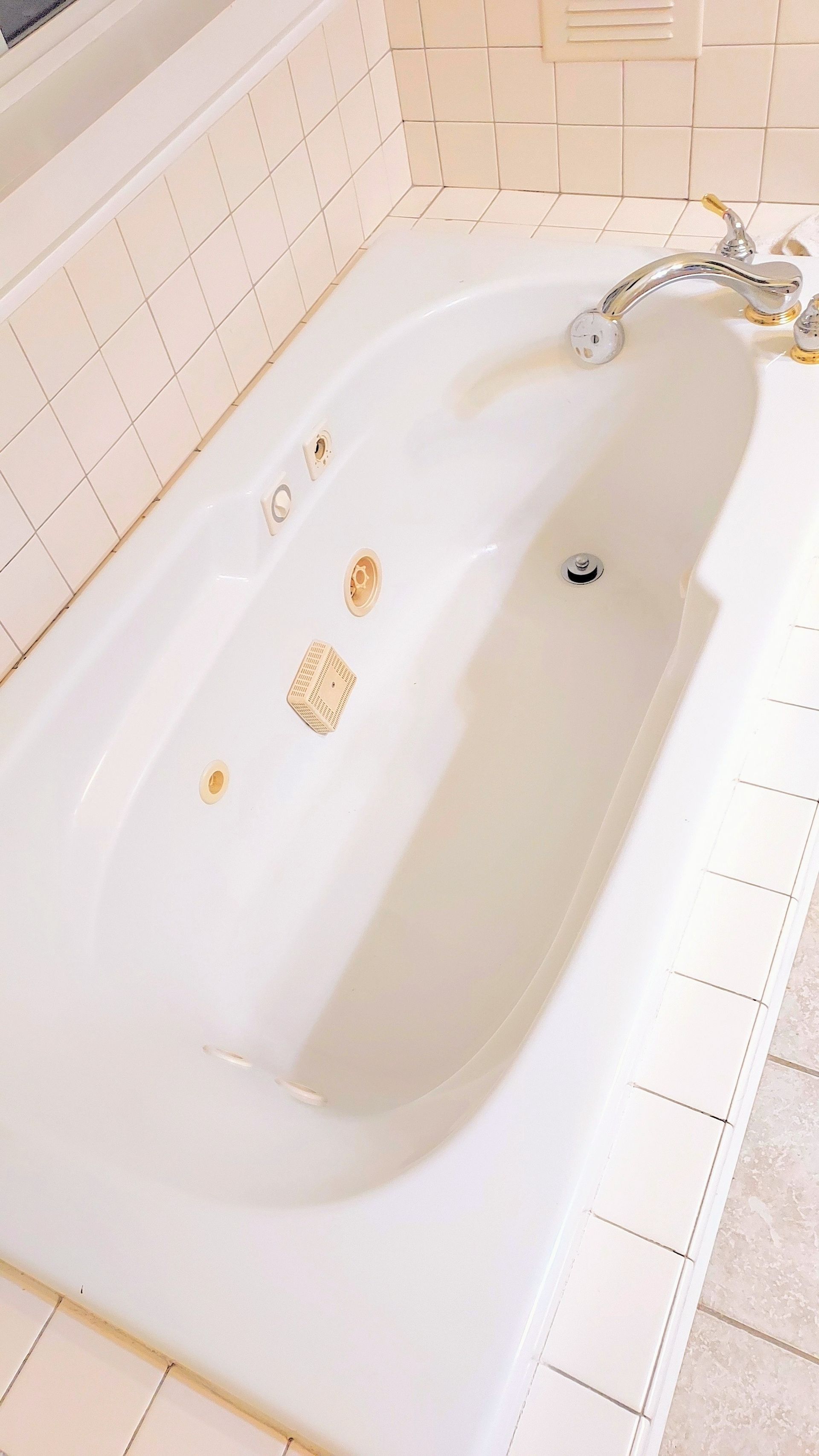 White bathtub with rust-colored stains and chrome fixtures, set in a tiled bathroom.