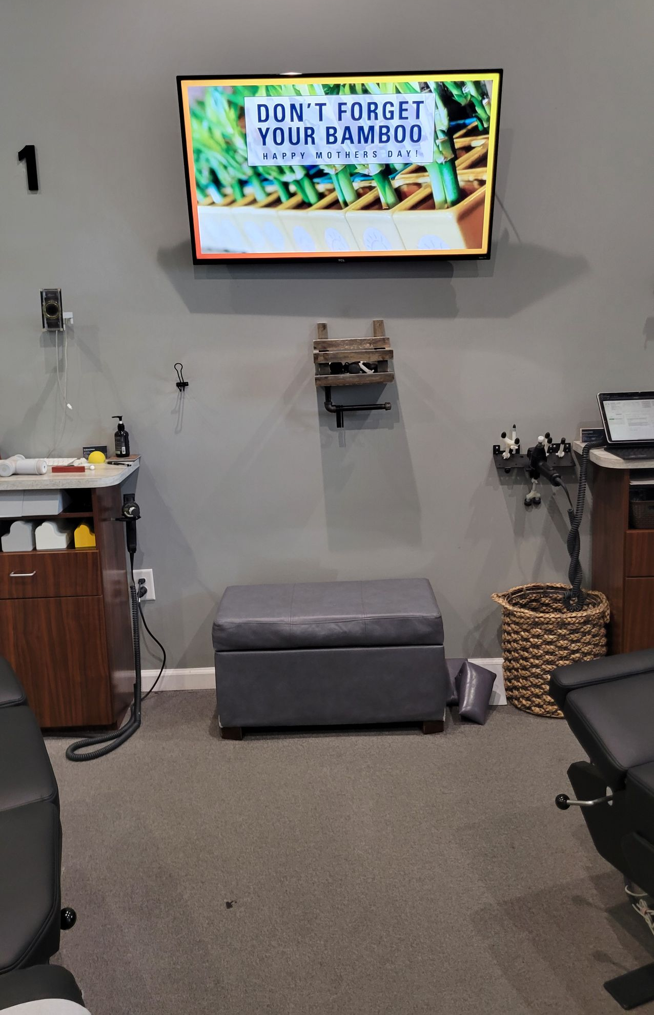 Interior of a chiropractic office with a TV displaying text, a gray storage ottoman, and various medical equipment.
