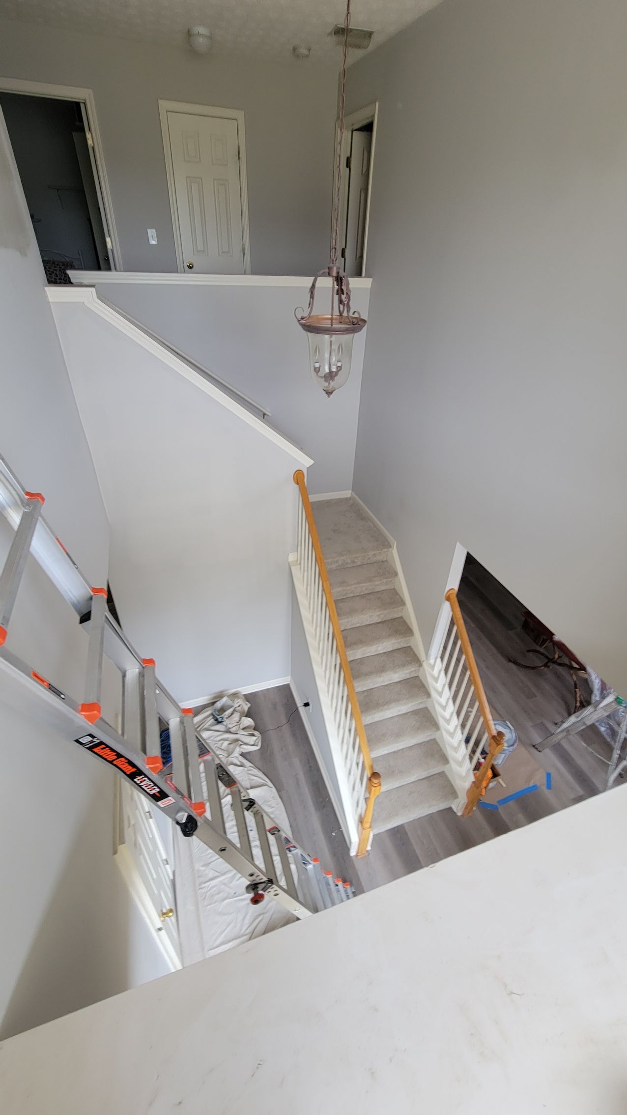 Staircase in a home with freshly painted walls. A ladder leans against a wall, and doors are visible.
