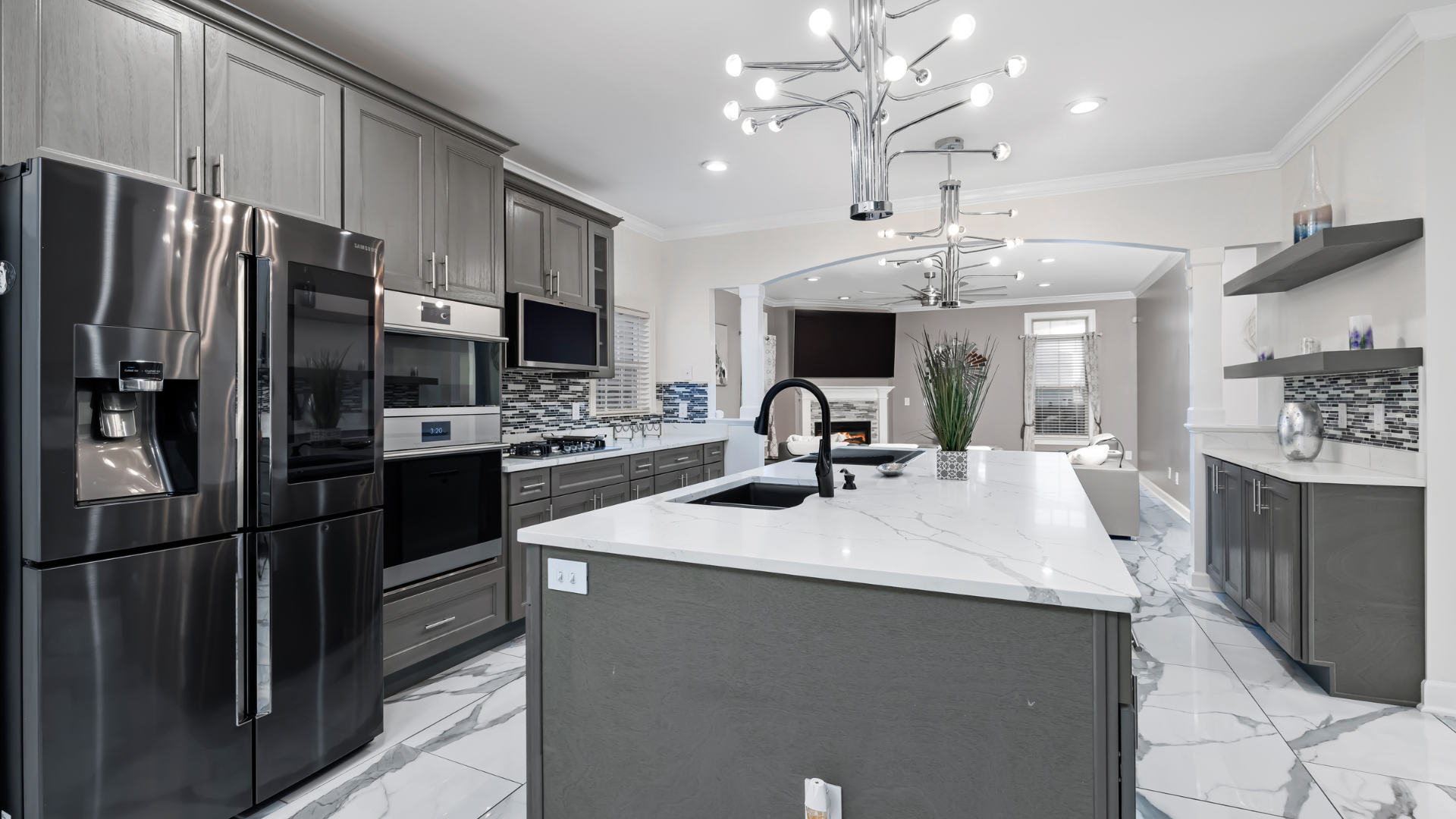 Modern gray kitchen with stainless steel appliances, large island, and marble floors.