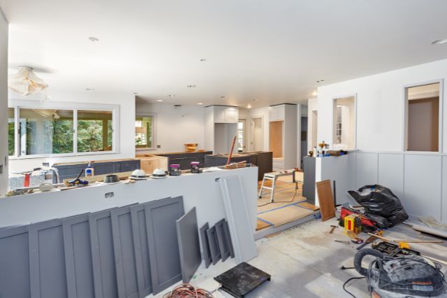 Kitchen undergoing renovation, with gray cabinets, tools, and construction materials scattered around.