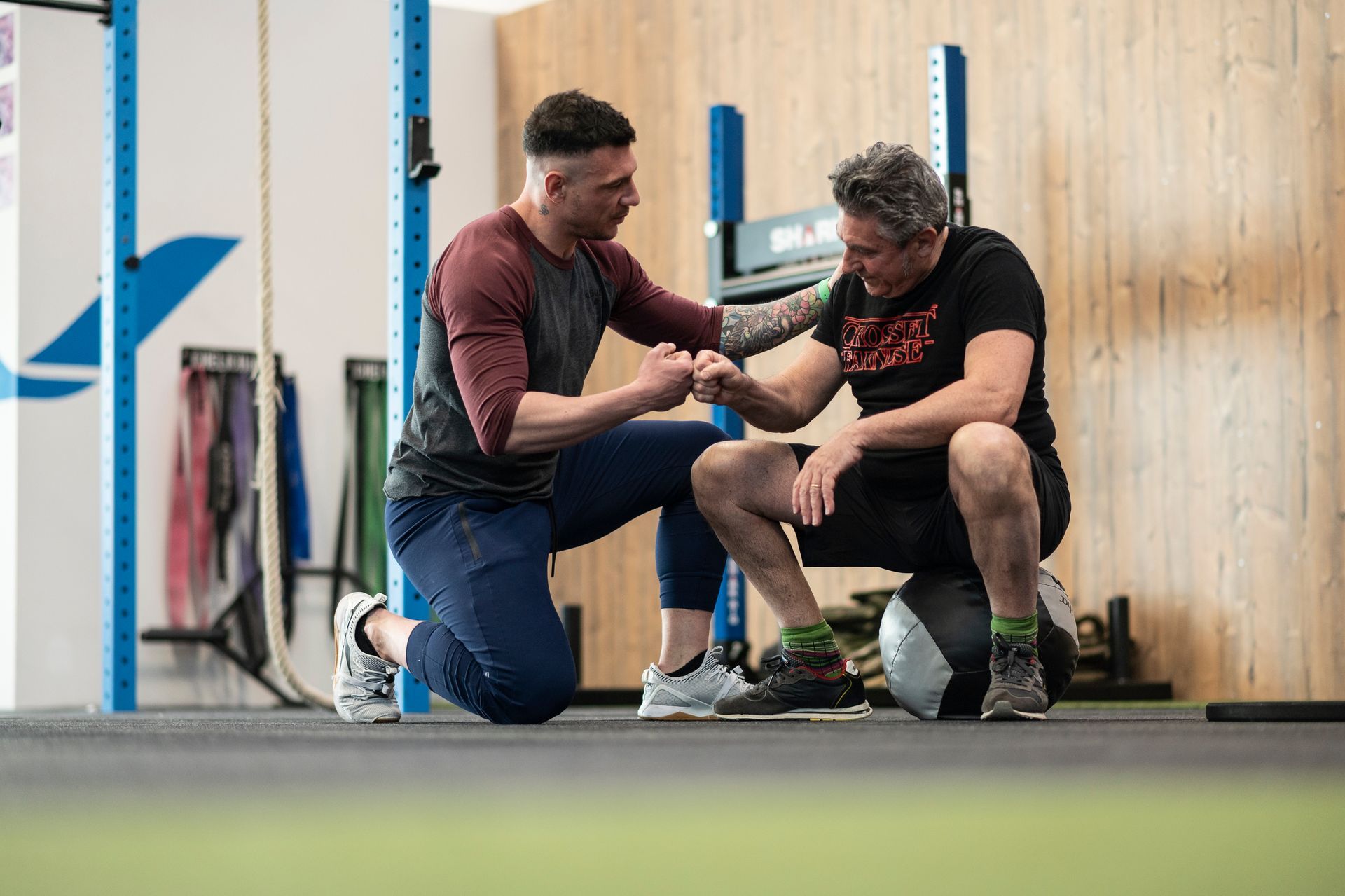 A man is squatting down next to another man in a gym.