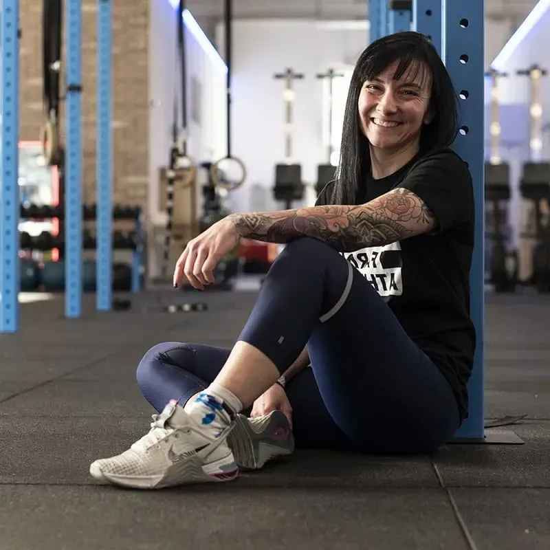 A woman is sitting on the floor in a gym wearing nike shoes