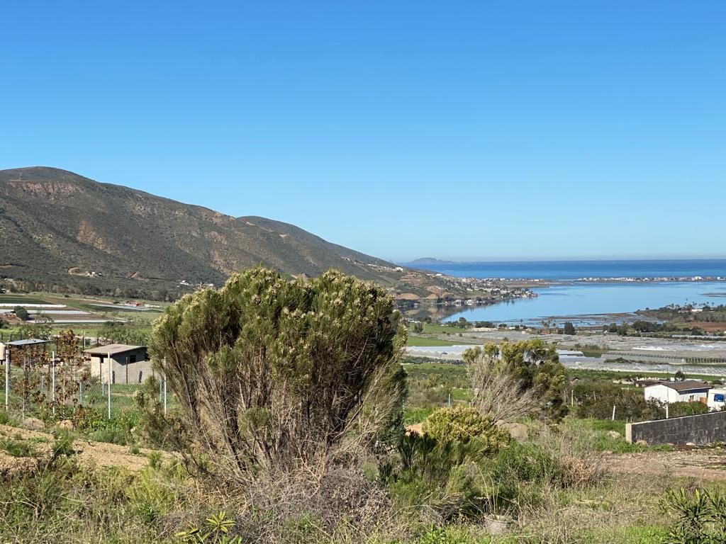 A scenic view of Pacific ocean coastal area with mountains, water, and buildings under a clear blue sky.