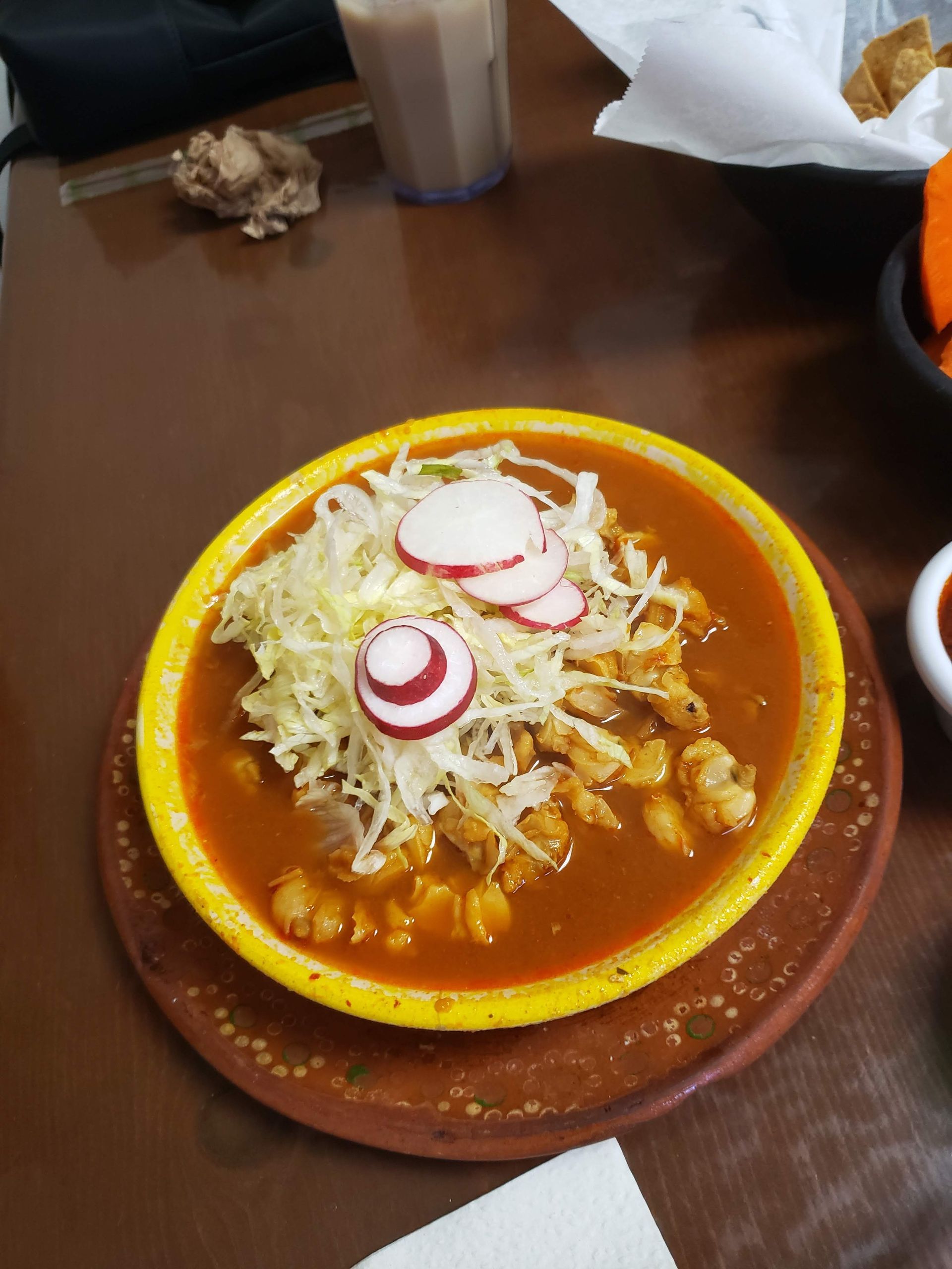 Pozole soup in yellow bowl, topped with cabbage and radishes, on a table.