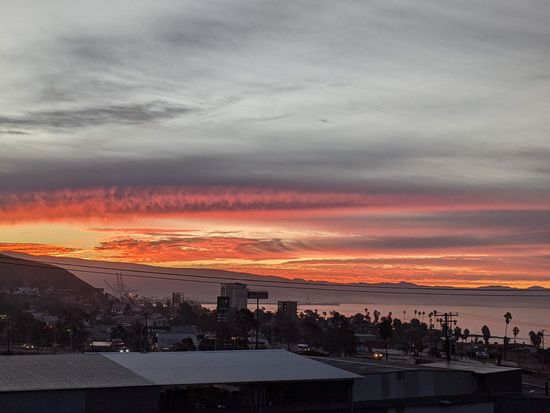 Sunset over a coastal city with colorful sky and silhouetted buildings.