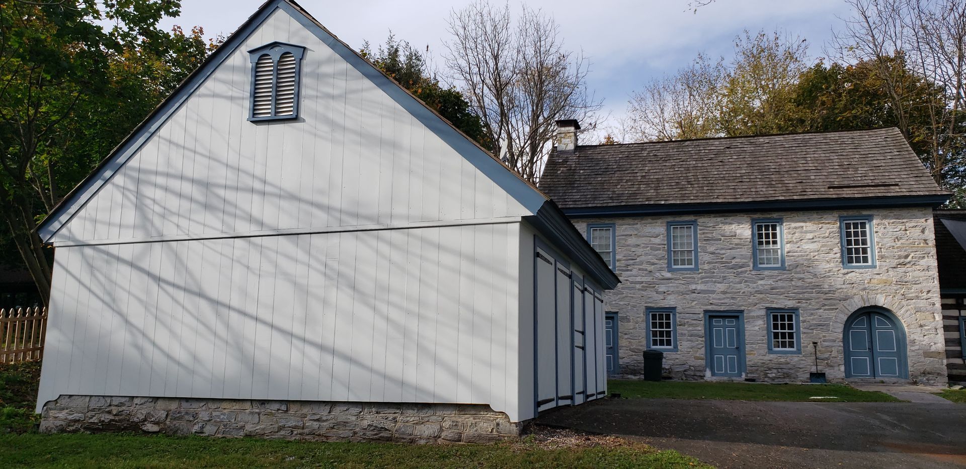 White farmhouse and stone building with arched doorway under a partly cloudy sky