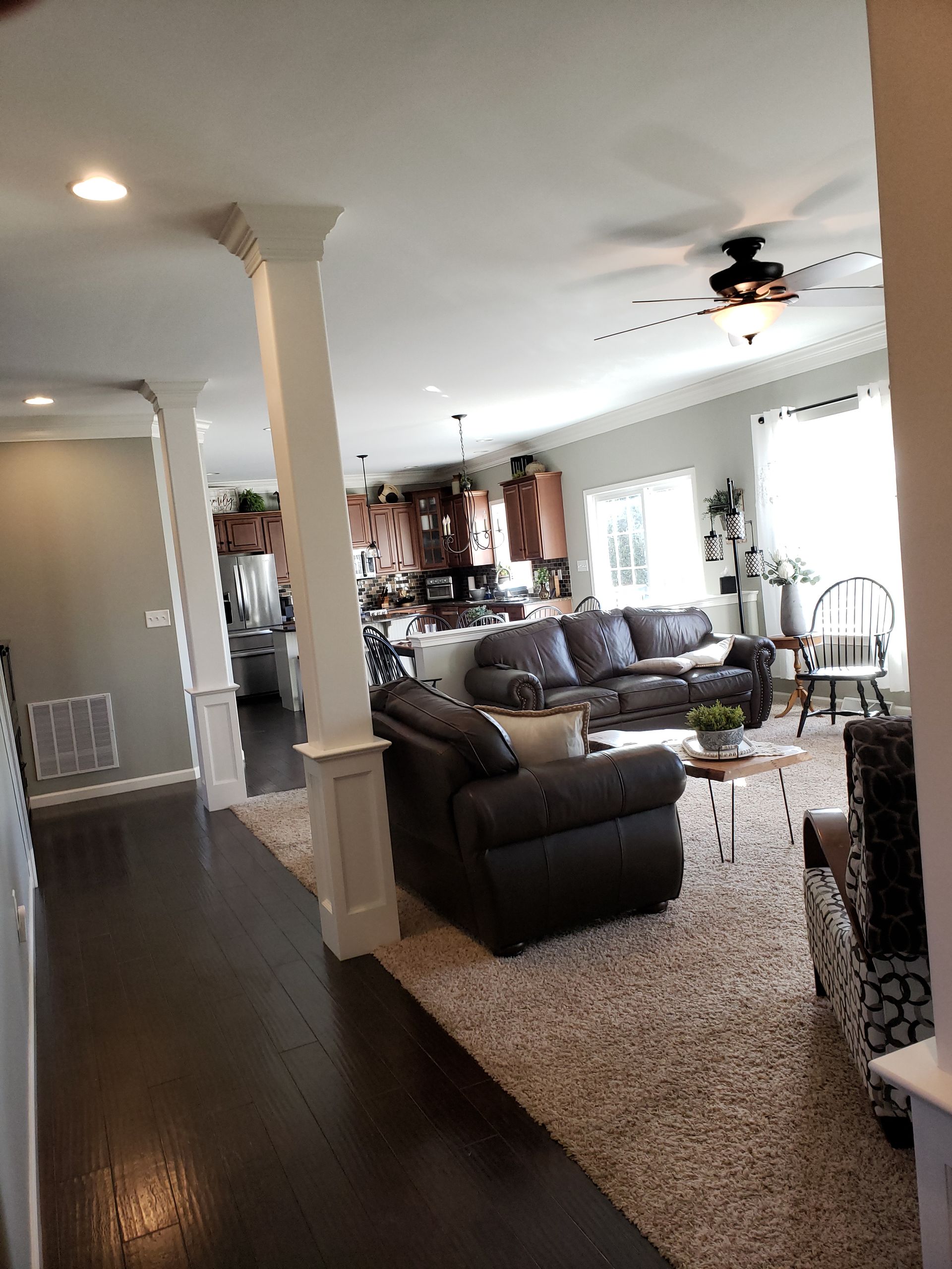 Open living room with dark wood floors, gray sofas, white columns, and a ceiling fan