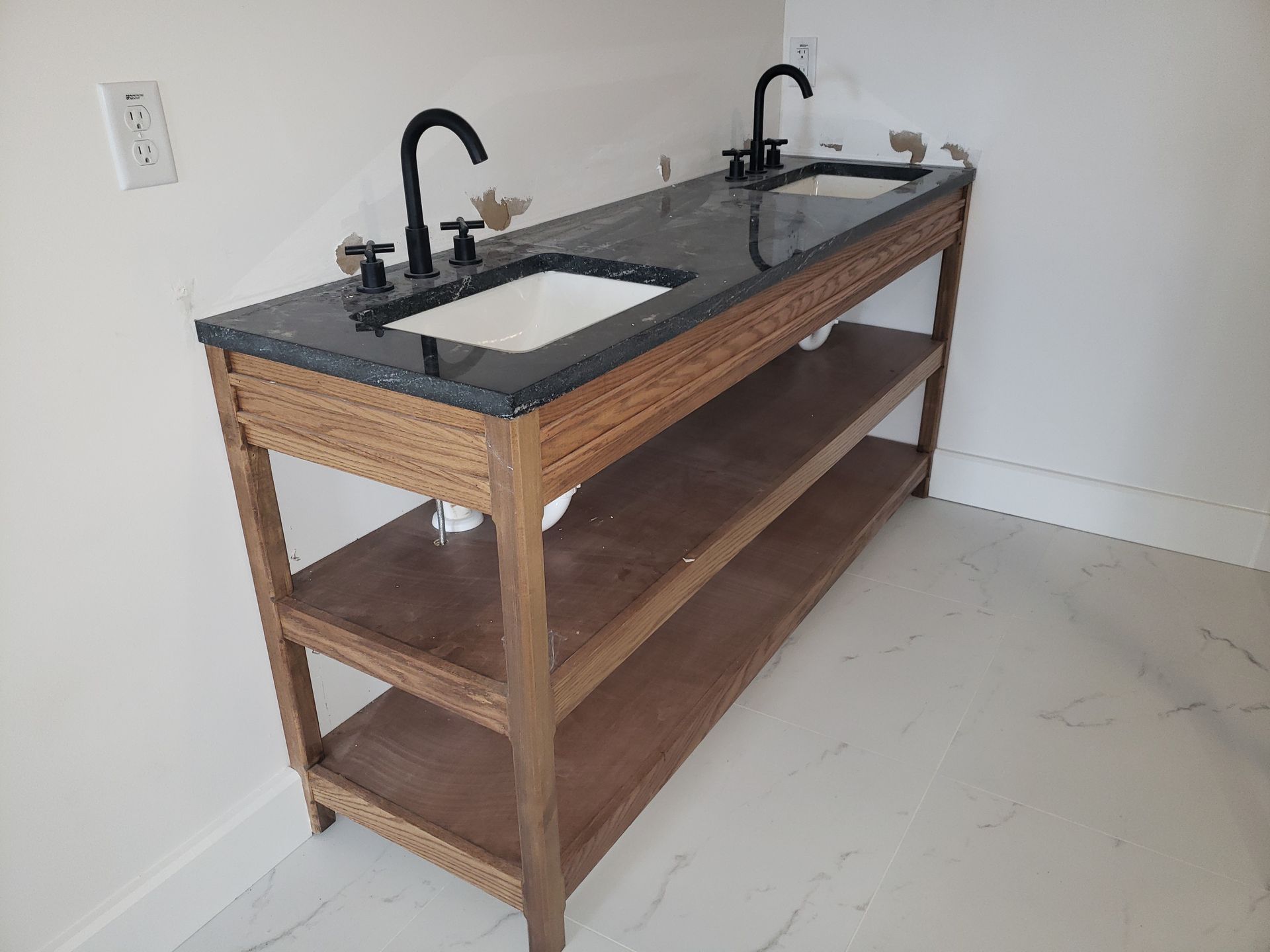 Wooden double sink vanity with black countertop in an unfinished bathroom room